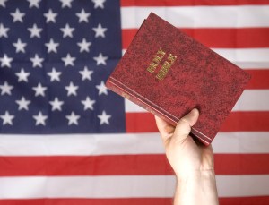 Upraised hand holding a bible in front of a flag