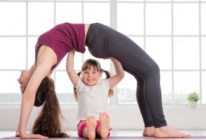 Young mother and daughter doing yoga exercise in fitness studio with big windows on background